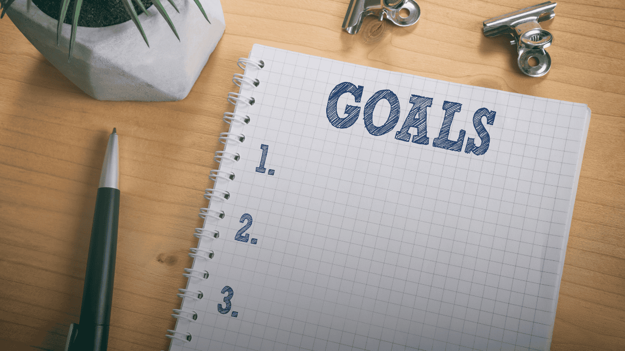 Open notebook on a wooden desk with 'GOALS' stamped at the top and a numbered list, representing simplified planning and setting clear actions over complex resolutions.