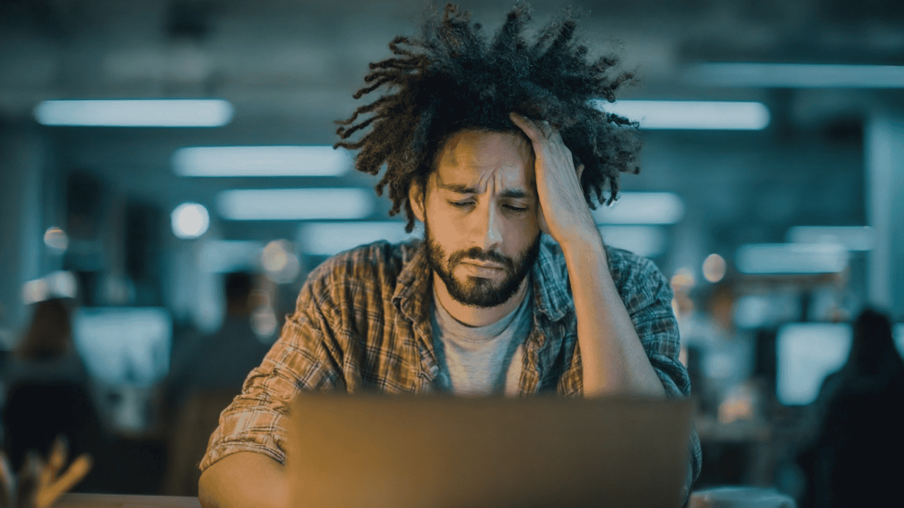 Exhausted employee staring blankly at a laptop in a dimly lit office, illustrating the physical toll of burnout and the fatigue that goes unnoticed in high-pressure environments.