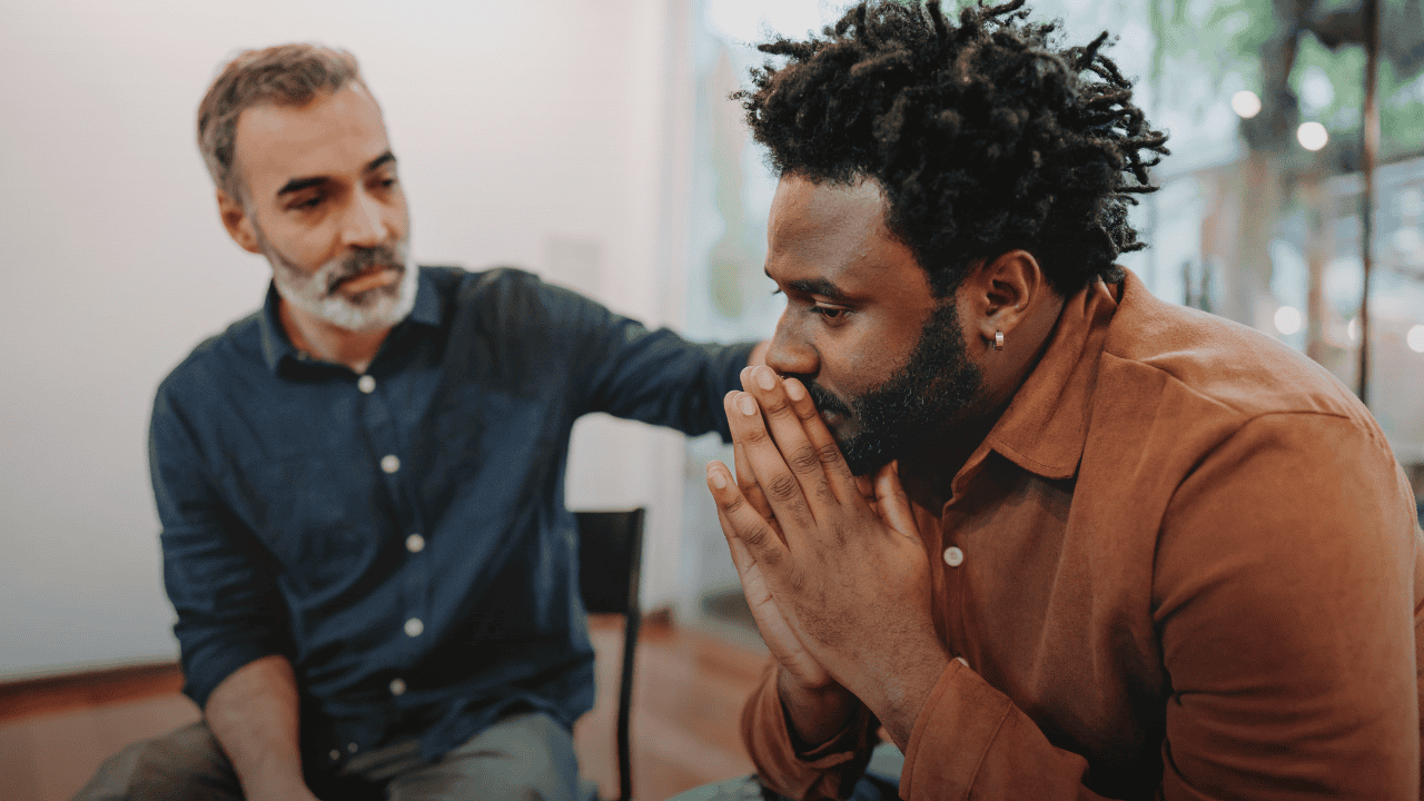 A colleague placing a supportive hand on the shoulder of a distressed man, demonstrating how peer support can break the silence and offer psychological safety.