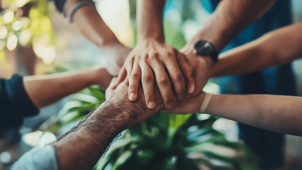 A group stacking hands in unity, representing mental wellness built on community support and compassion rather than self-judgment.