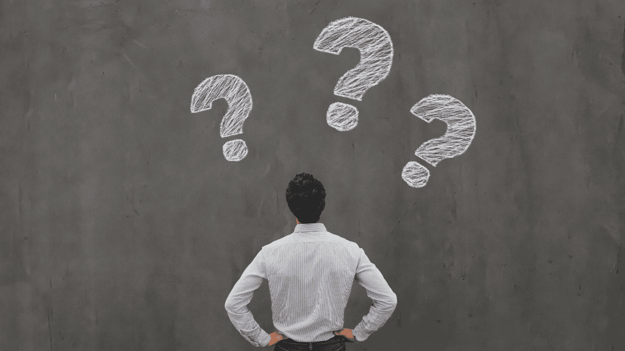 A man looking at question marks on a wall, symbolizing the power of asking questions and where personal growth begins.