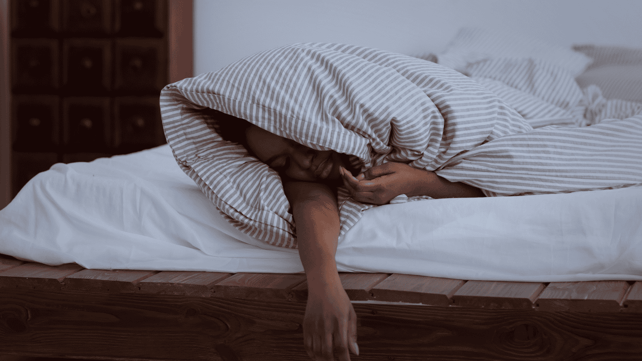 A woman struggling with insomnia, resting her head under a pillow, representing common sleep disruptions and mental fatigue.
