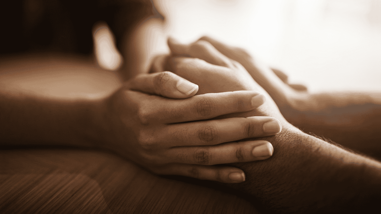 A supportive gesture showing one person gently holding another’s hands, representing psychological safety, human connection, and communal healing after a tragedy.