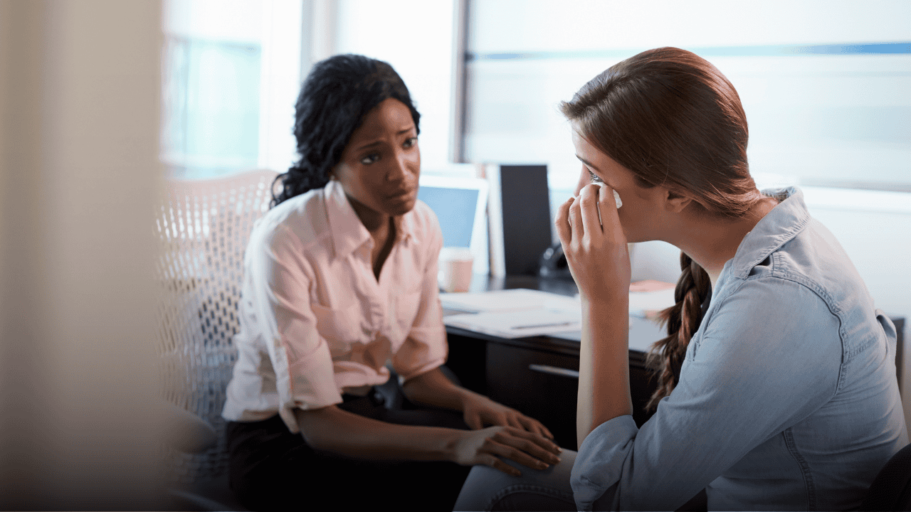 An empathetic manager actively listening and comforting an emotional colleague wiping away tears in an office, demonstrating psychological safety and supportive leadership.